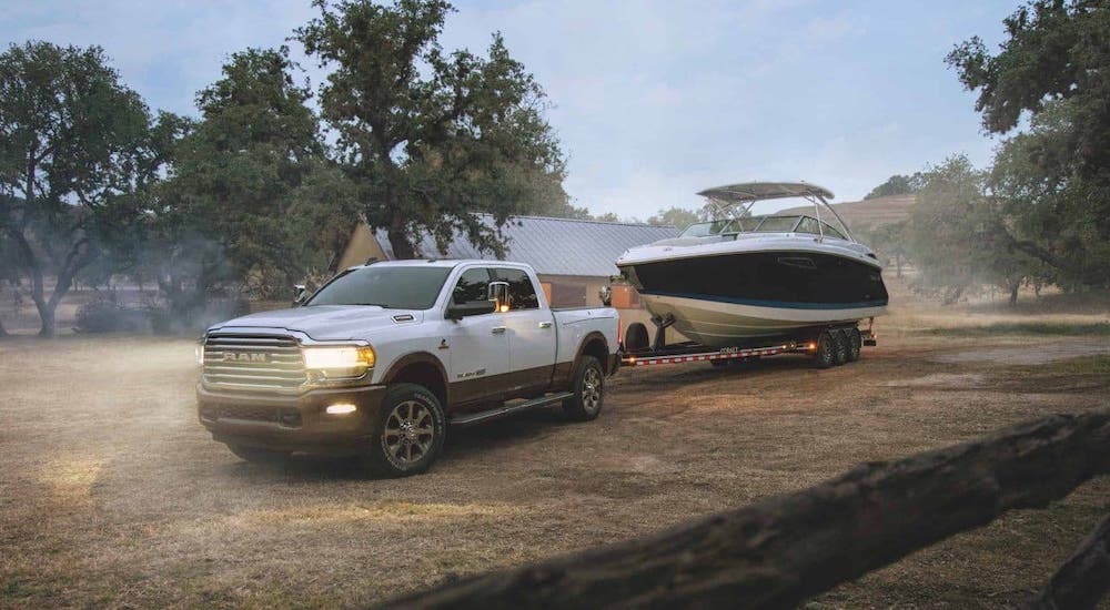 A white 2020 Ram 2500 is towing a boat on a dirt road at dusk.