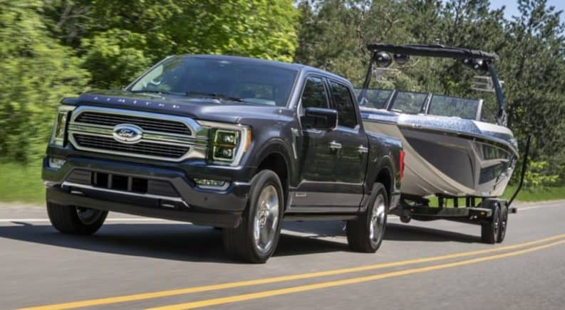 A black 2021 Ford F-150 is towing a boat past trees.