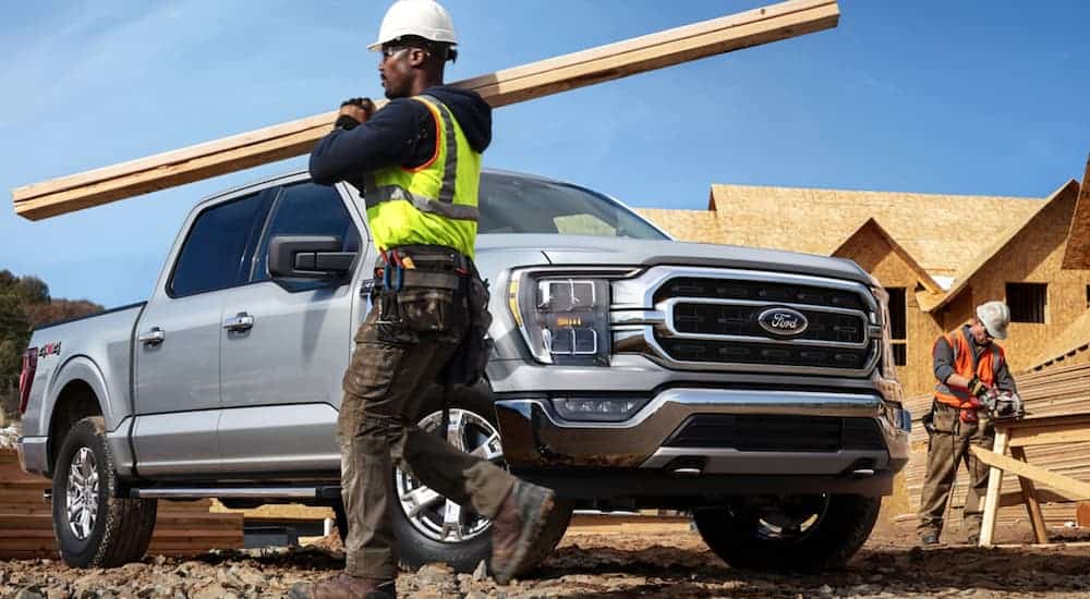 A silver 2021 Ford F-150 is at a construction site while workers build a house.
