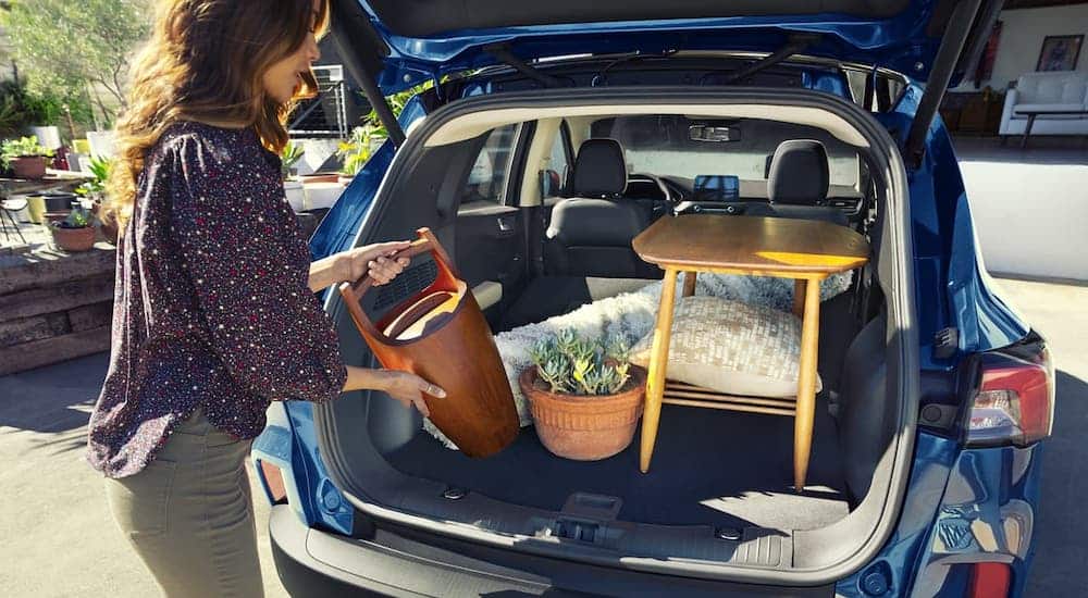 A woman is loading home goods into the cargo area of a blue 2020 Ford Escape.