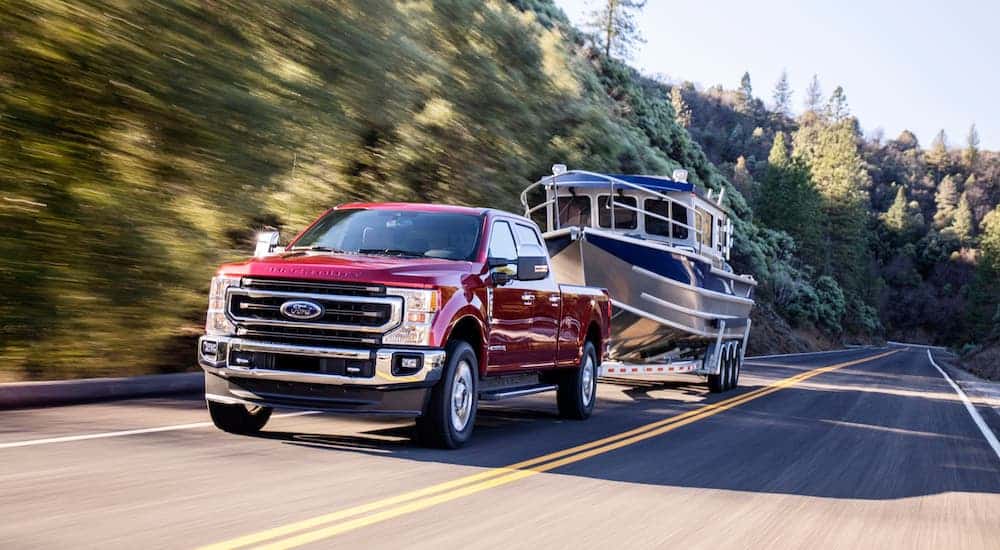 A red 2020 Ford F-250 King Ranch is towing a boat on a highway.