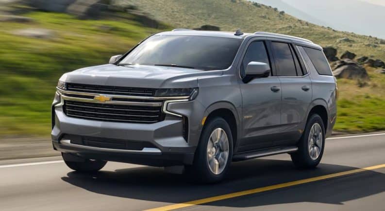 A grey 2021 Chevy Tahoe, which is a popular topic in current auto news, is driving past grassy hills.