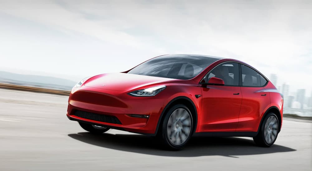 A red 2021 Tesla Model Y is driving away from a hazy city.