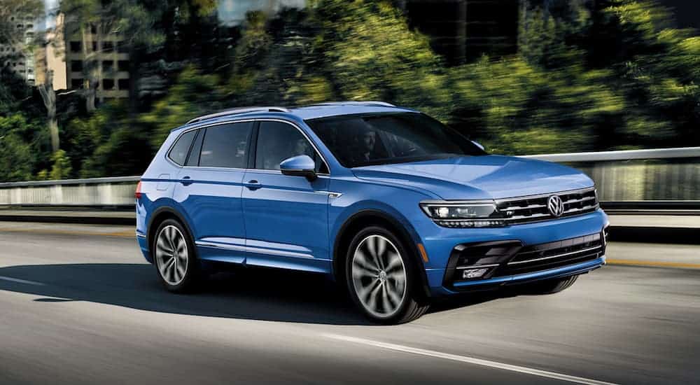 A blue 2020 Volkswagen Tiguan is driving on a highway through a city.