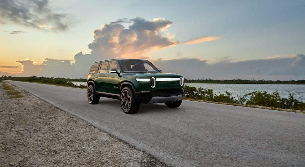 A green Rivian R1S is driving on a highway next to a lake.