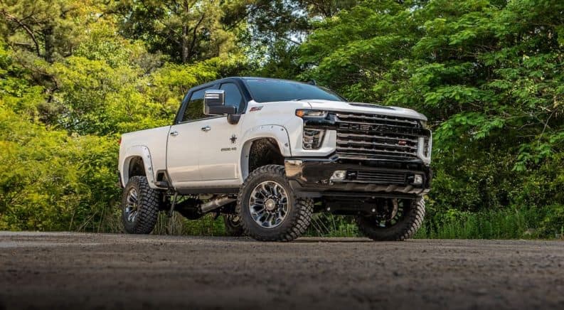 A white Chevy Silverado 2500HD Black Widow from SCA Performance is parked in front of trees.