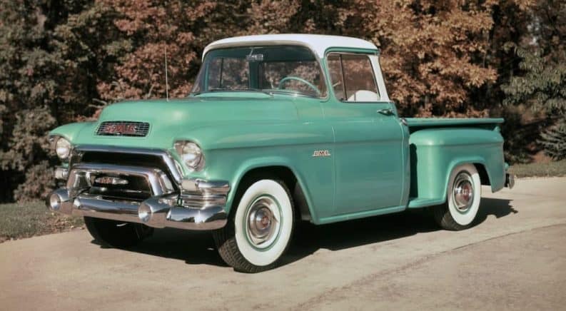 A teal 1955 GMC 100 Series Deluxe is in front of trees.