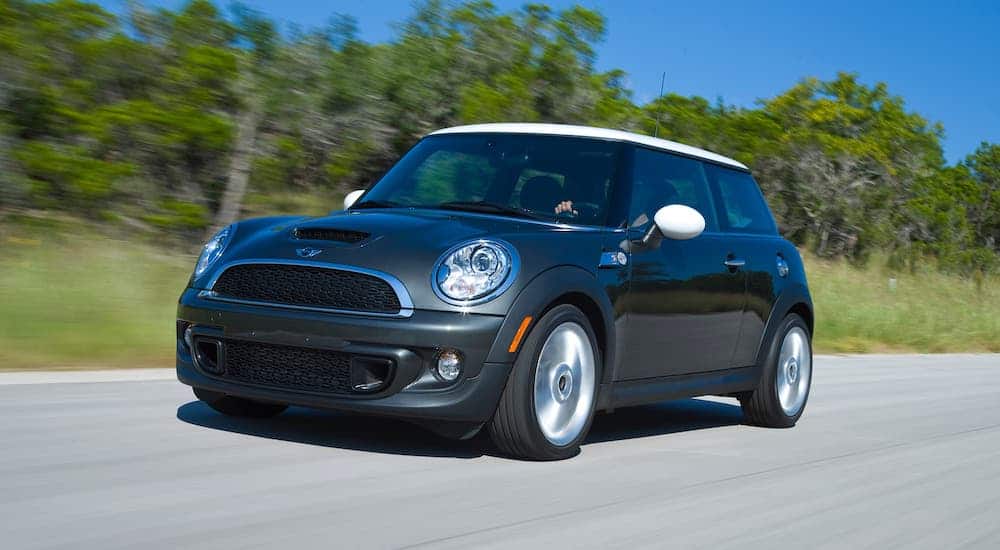 A black 2011 MINI Cooper Hardtop is driving in front of trees and a blue sky.