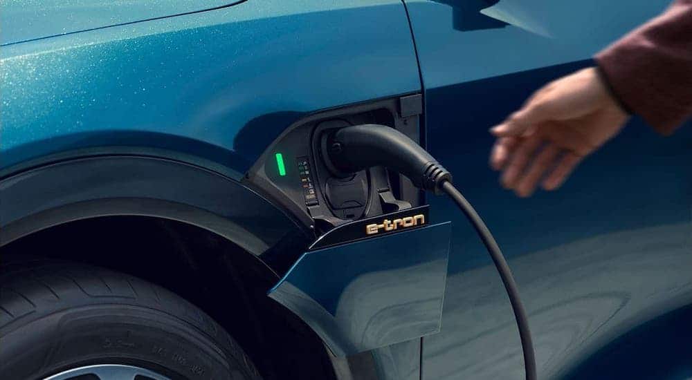 A closeup shows a hand reaching towards the charger on a blue 2019 Audi e-tron.