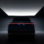 A silhouette of a 2019 Audi e-tron is shown from the rear in a dimly lit room.
