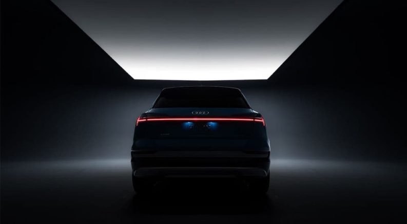 A silhouette of a 2019 Audi e-tron is shown from the rear in a dimly lit room.