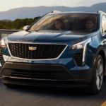 A blue 2020 Cadillac XT4 is driving past a bridge and mountains after winning the 2020 Cadillac XT4 vs 2020 Volvo XC40 comparison.