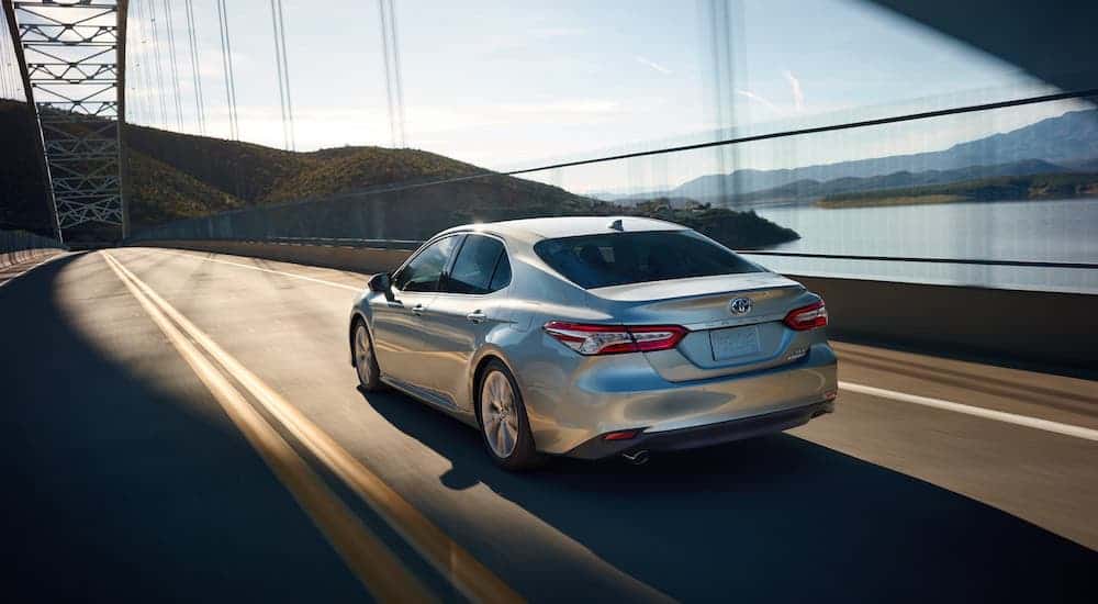 A silver 2020 Toyota Camry is driving on a bridge over a river.