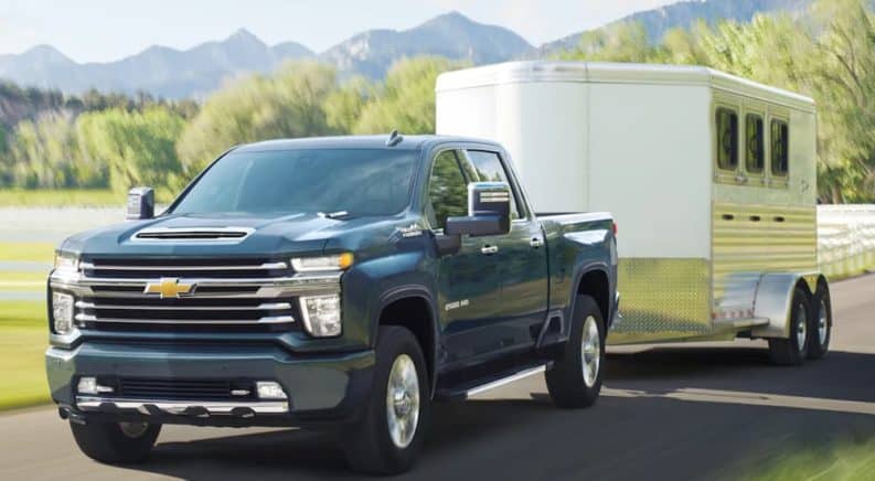 A blue 2020 Chevy Silverado 2500HD is towing a white enclosed trailer past mountains.