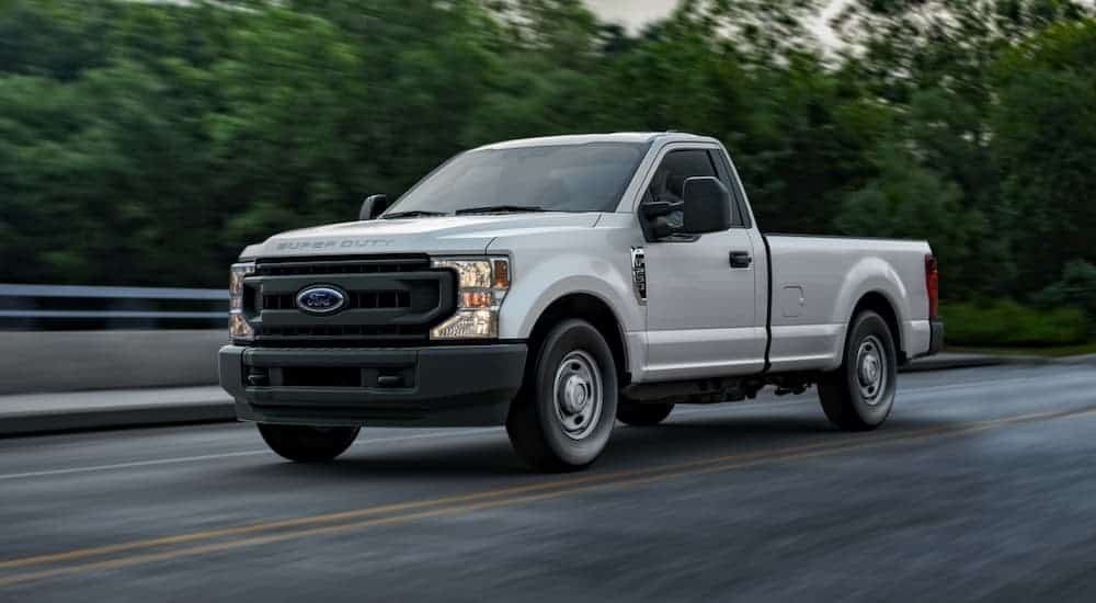 A white 2020 Ford F-250 Work Truck is driving past trees.