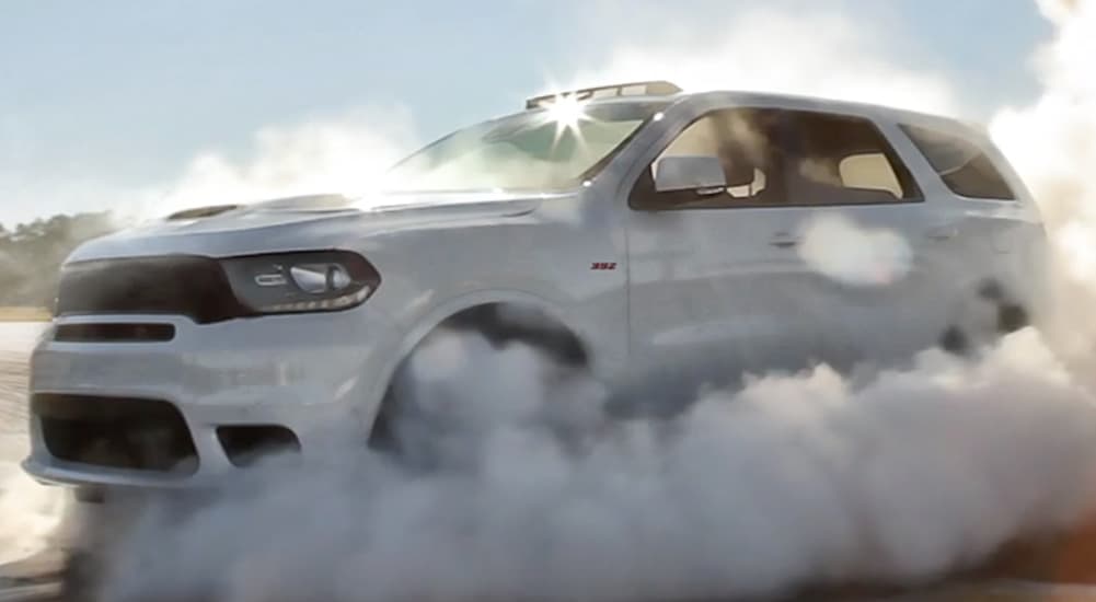 A white 2020 Dodge Durango SRT is doing a burnout in a cloud of smoke.