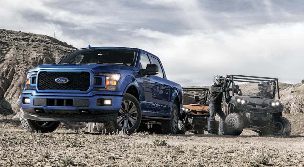 A blue 2020 Ford F-150 is parked off-road next to side-by-sides.