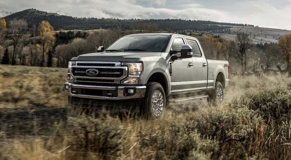 A silver 2020 Ford F-250 is driving through a field with distant hills.
