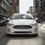 A white 2020 Ford Fusion is shown from the front while driving in a city.