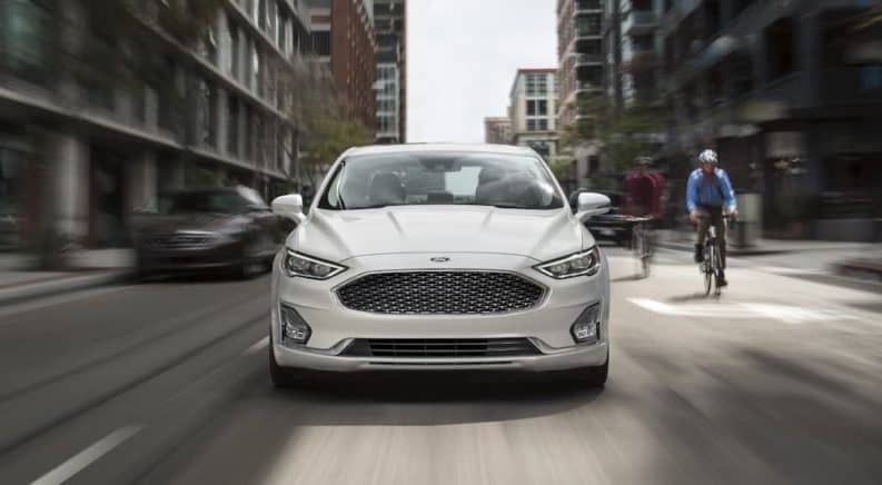 A white 2020 Ford Fusion is shown from the front while driving in a city.