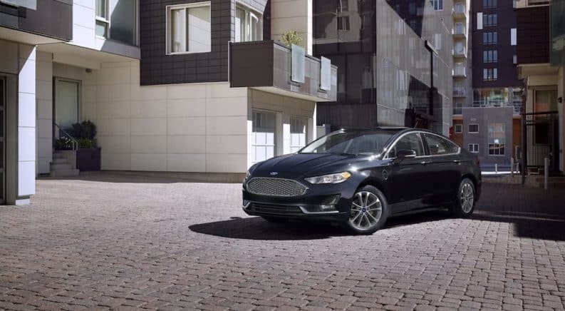 A black 2020 Ford Fusion Hybrid is parked in front of modern buildings in a city.