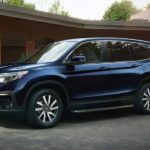 A blue 2021 Honda Pilot is parked in front of a modern wood home.