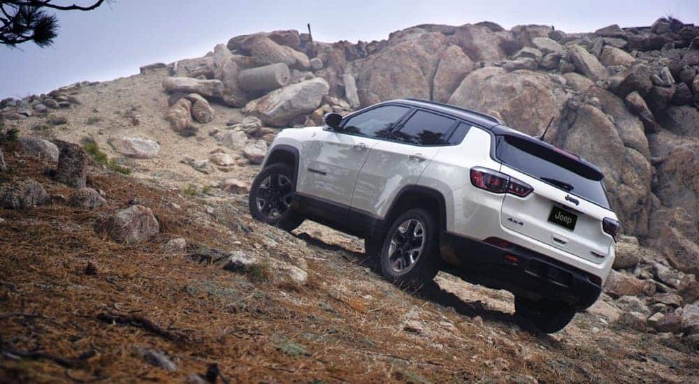 A white 2020 Jeep Compass Trailhawk is shown climbing a rocky hill.