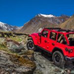 A red 2020 Jeep Wrangler Unlimited is off-roading up a rocky mountain after winning the 2020 Jeep Wrangler Unlimited vs 2020 Toyota 4Runner comparison.