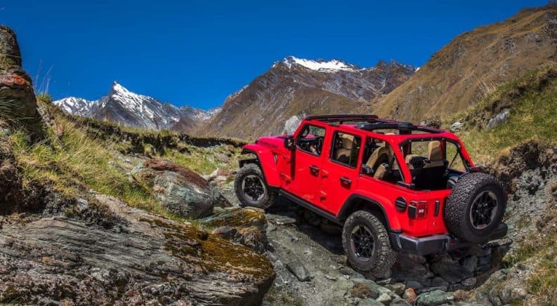 A red 2020 Jeep Wrangler Unlimited is off-roading up a rocky mountain after winning the 2020 Jeep Wrangler Unlimited vs 2020 Toyota 4Runner comparison.