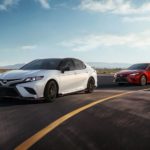 A white and a red 2020 Toyota Camry are driving on a race track.