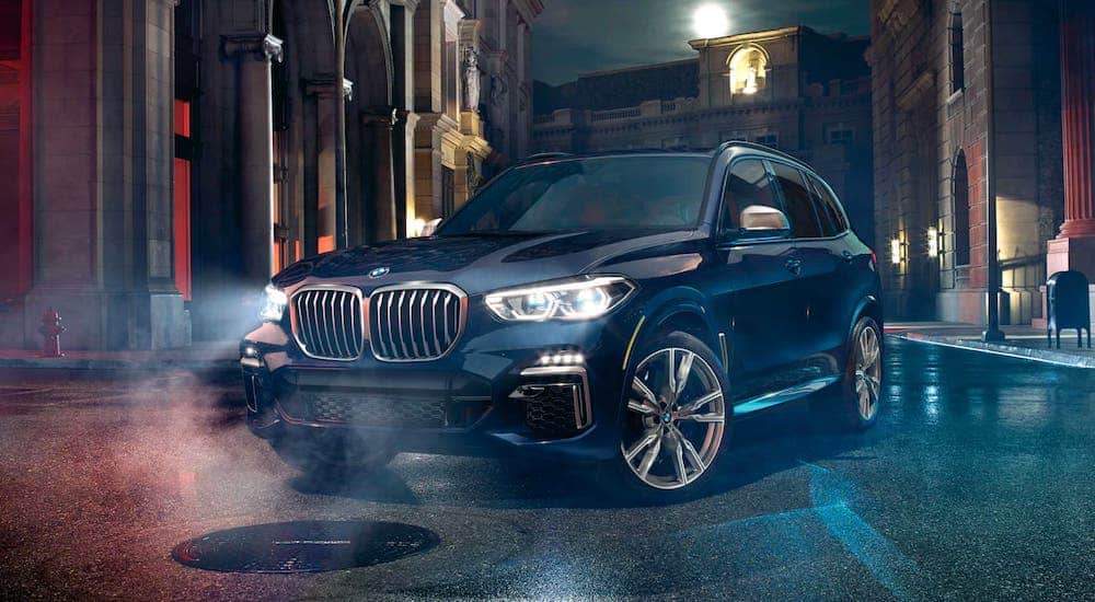 A black 2021 BMW M Series X5 is parked in an alleyway at night.