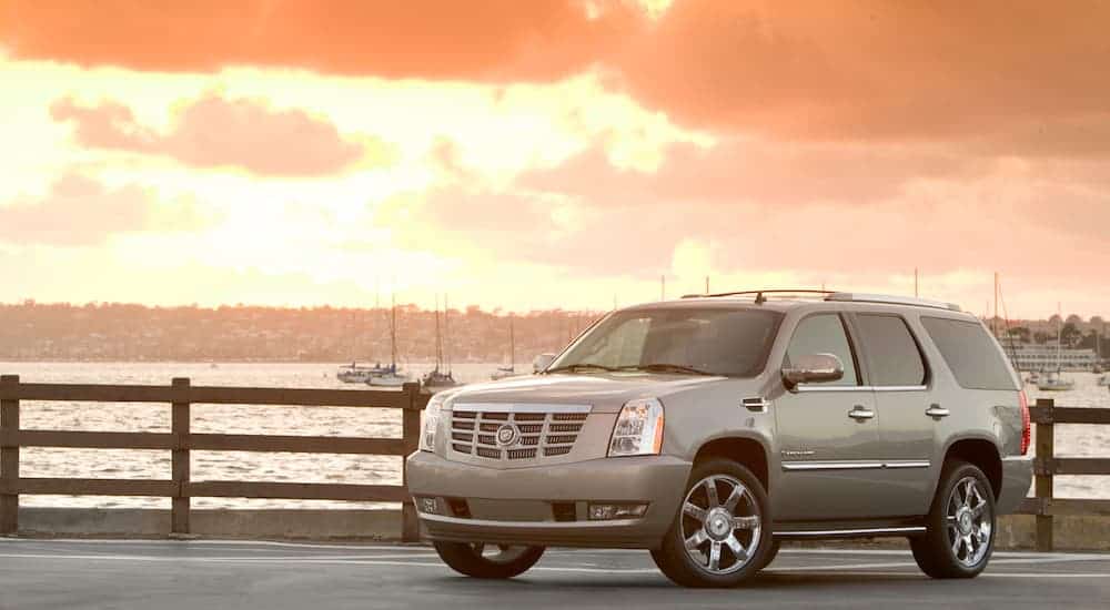 A tan 2009 Cadillac Escalade is parked in front of the ocean at sunset.
