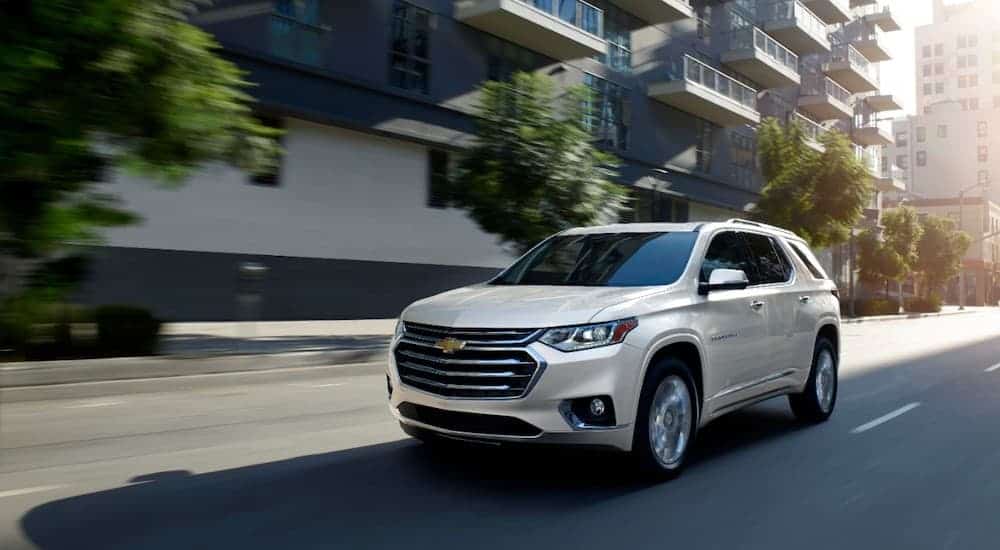 A white 2020 Chevy Traverse High Country is driving on a city street after leaving a car dealership near me.
