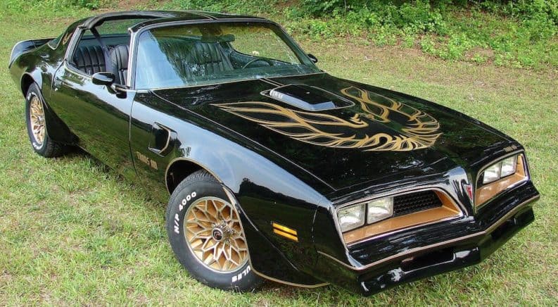 A black 1977 Pontiac Trans Am is shown parked on the grass of a used car dealership near me.