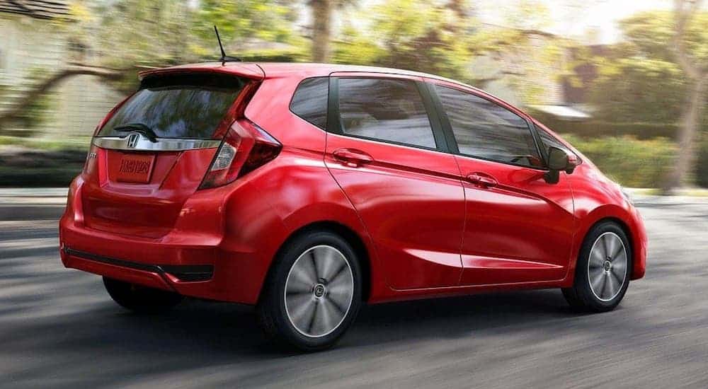 A red 2020 Honda Fit is driving on a suburban road.