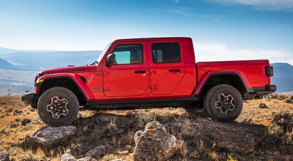 A red 2020 Jeep Gladiator is shown from the side while off-roading over rocks.