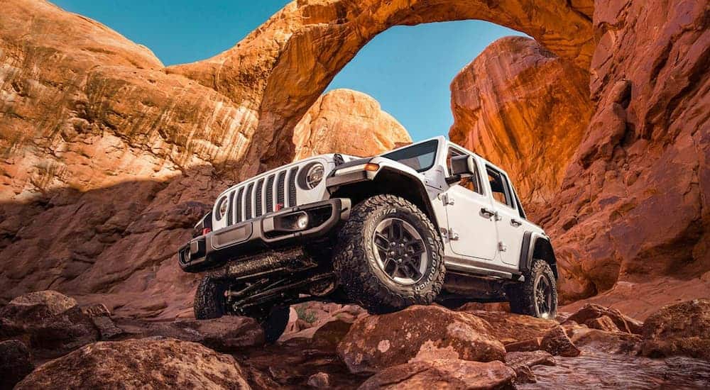 One of the most popular Jeep models, a white 2020 Jeep Wrangler Unlimited, is parked on red rocks while off-roading.