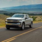 A popular truck for sale, a silver 2020 Chevy Silverado 1500, is driving on a rural highway.