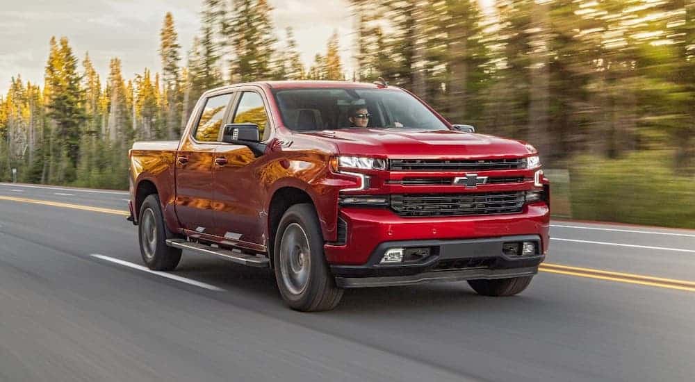 A red diesel 2020 Chevy Silverado 1500 is driving on a woodland highway.