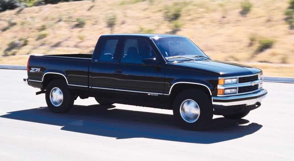 A popular used Chevy truck, a black 1999 Chevy Silverado, is driving on a highway.