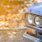A blue 1970 Nissan Datsun 510 is parked and showing a close up of one headlight.