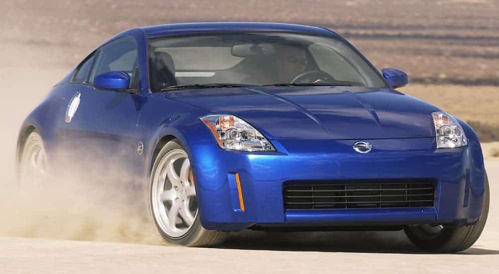 A blue 2007 Nissan 350Z is driving in the dirt and kicking up dust.