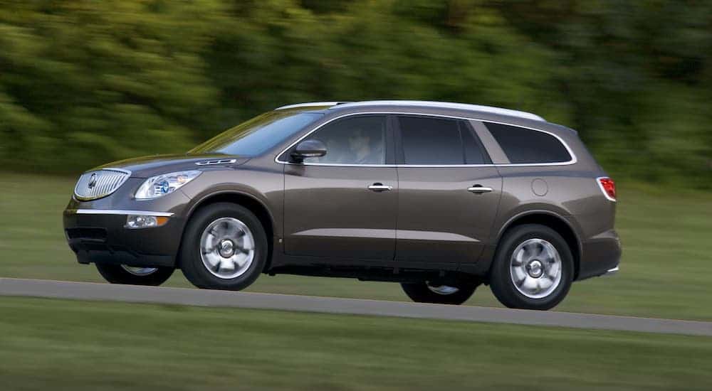A gray 2009 Buick Enclave is driving on a rural road and shown from the side.