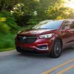 A red 2020 Buick Enclave SportTouring is driving on a tree-lined highway.