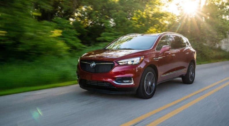 A red 2020 Buick Enclave SportTouring is driving on a tree-lined highway.