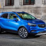 A blue 2020 Buick Encore is parked in front of an older concrete building.
