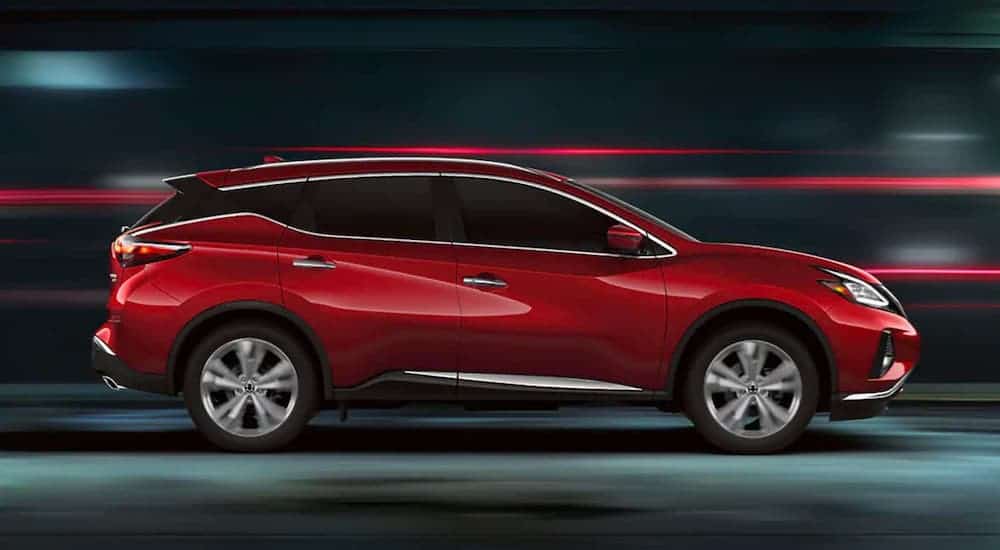 A red 2020 Nissan Murano is shown from the side driving on a city street at night.