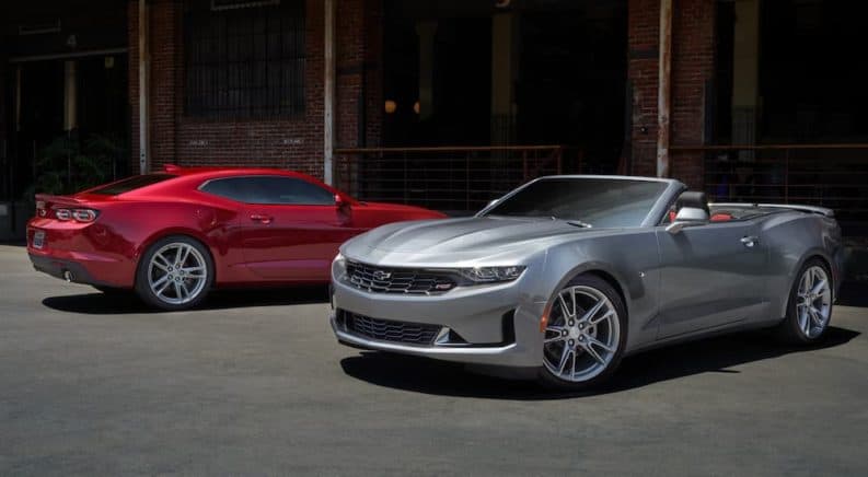A red 2020 Chevy Camaro and a silver convertible model are parked in front of brick building.