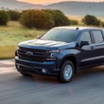 A blue 2020 Chevy Silverado RST is driving on highway with mountains in the distance.