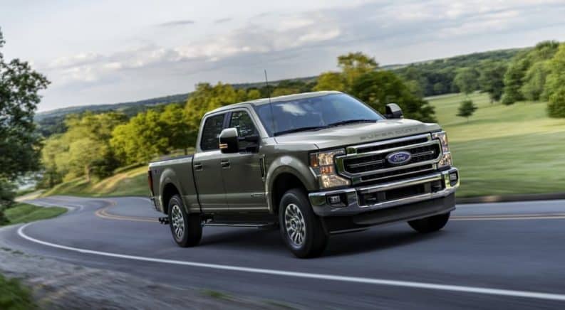 A grey 2020 Ford F-250 is driving on a winding road past trees after winning the 2020 Ford F-250 vs 2020 Chevy Silverado 2500HD comparison.